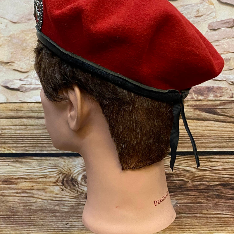 „Seitliche Ansicht von rotem Vintage Uniform-Barett mit schwarzem Rand und Zugband“