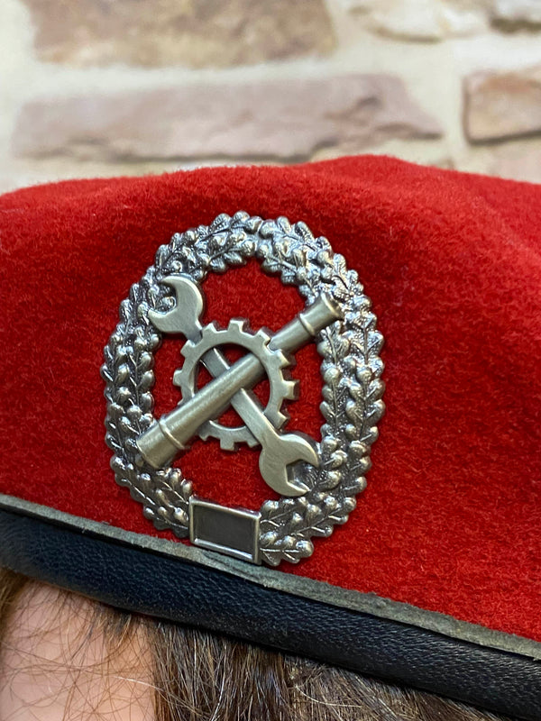 „Detailaufnahme vom silberfarbenen Metallabzeichen auf rotem Vintage Uniform-Barett“