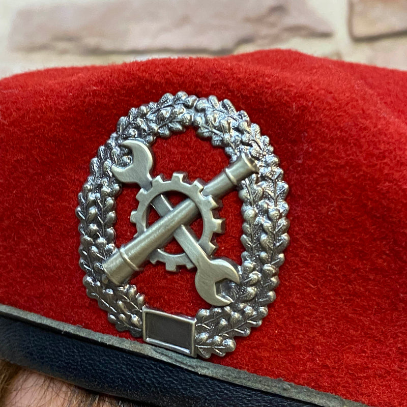 „Detailaufnahme vom silberfarbenen Metallabzeichen auf rotem Vintage Uniform-Barett“
