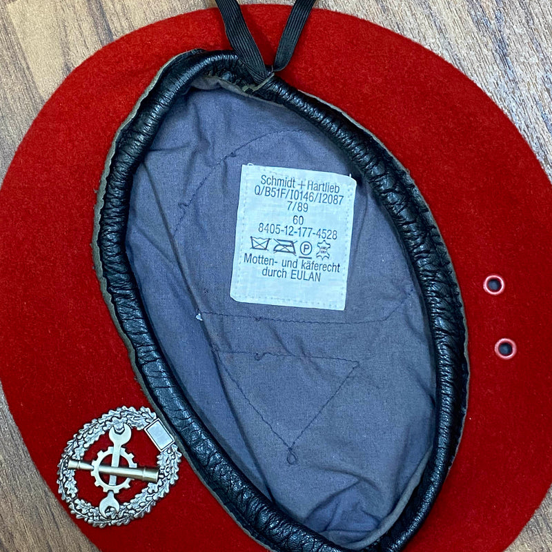 „Innenansicht eines roten Vintage Uniform-Baretts Größe 60 mit grauem Futter, Etikett und Metallabzeichen“