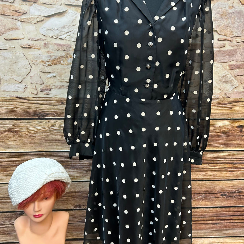 Vintage schwarzes Chiffonkleid mit weißen Tupfen, transparenten Puffärmeln und Hemdblusenkragen, dazu cremeweißer Cloche-Hut