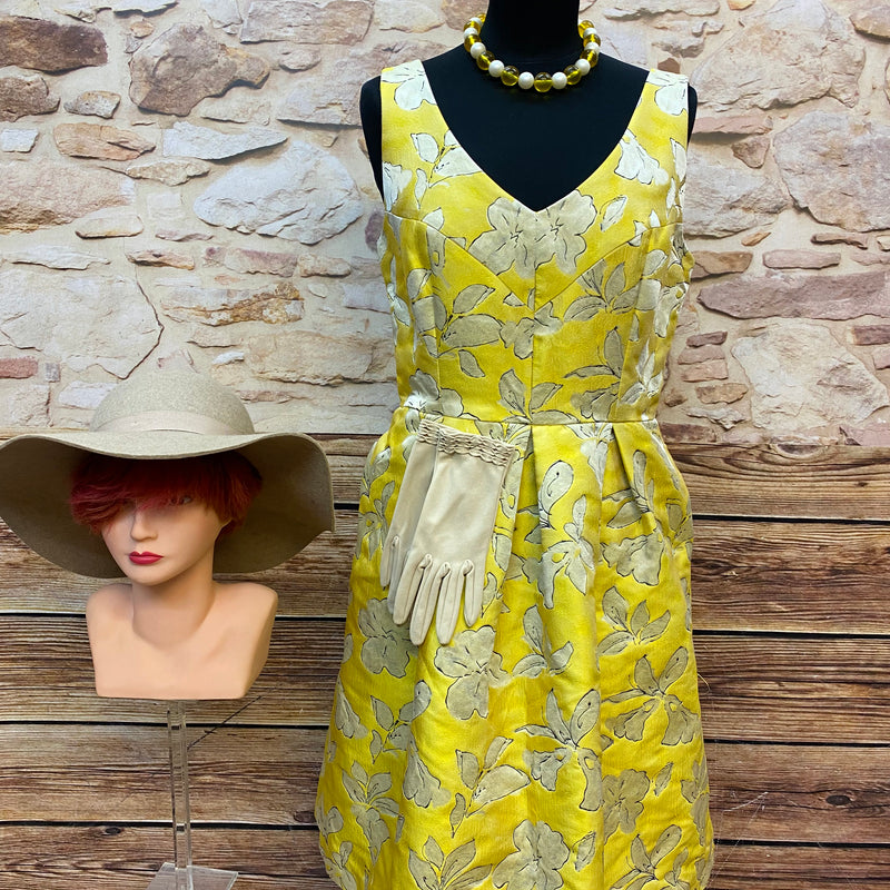 Gelbes Vintage Cocktailkleid im 50er Jahre Stil mit floraler Struktur, kombiniert mit Hut aus 100% Wolle, cremefarbenen Handschuhen und Perlenkette – komplettes Retro-Outfit.