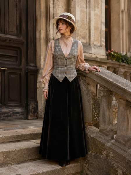 „Elegantes Vintage Damen Outfit mit langer Rock, Rüschenbluse, karierter Weste und Hut vor historischer Architektur“