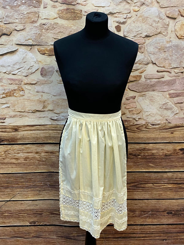 „Cremefarbene Vintage-Dirndlschürze mit Spitzenborten und Falten am Bund.“