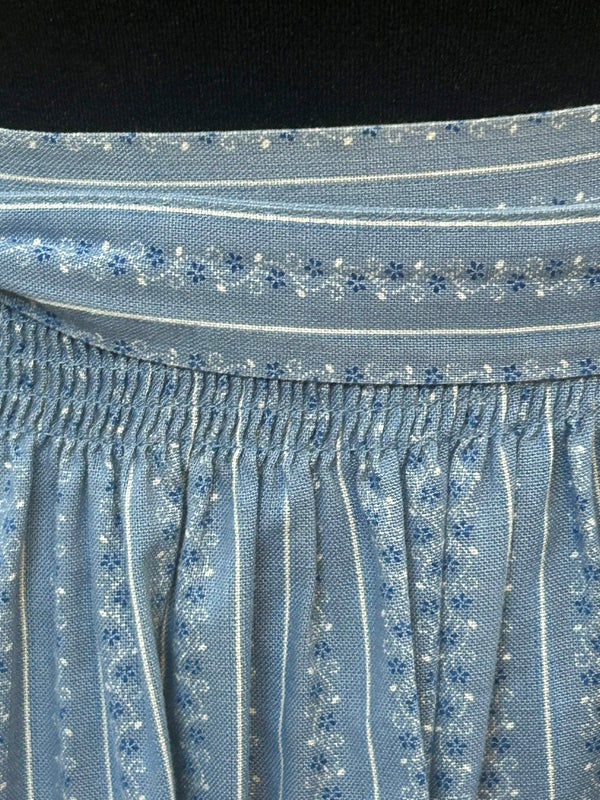 „Detailaufnahme Smokbund und Muster einer hellblauen Dirndl-Schürze im Vintage-Stil“