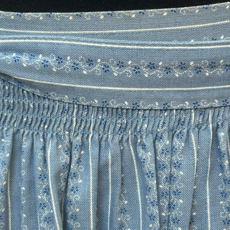 „Detailaufnahme Smokbund und Muster einer hellblauen Dirndl-Schürze im Vintage-Stil“