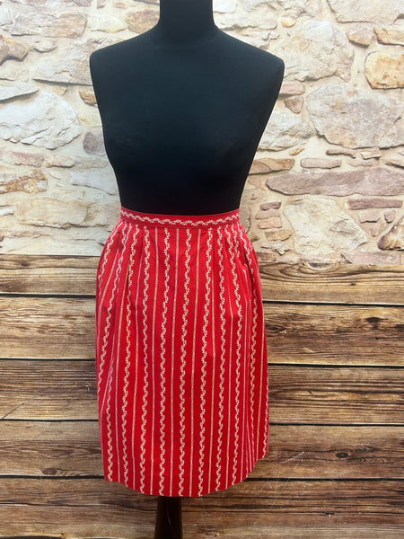 „Vintage Dirndl-Schürze in Rot mit weißem Streifendruck und Metallschließe, frontal auf Schneiderpuppe“