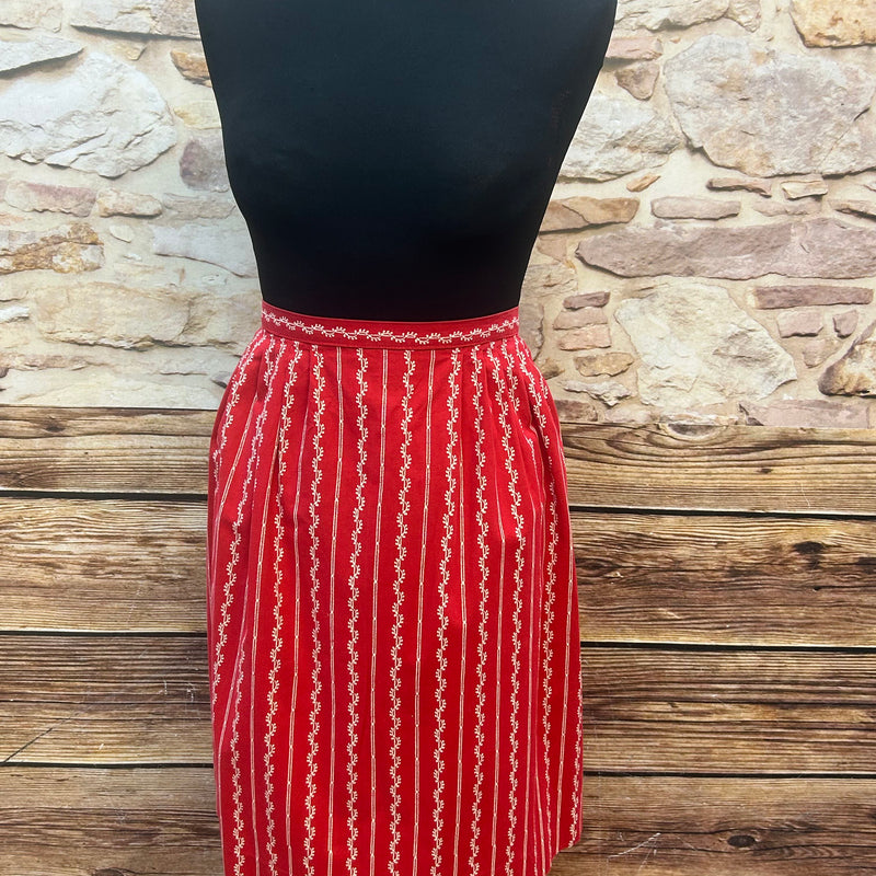 „Vintage Dirndl-Schürze in Rot mit weißem Streifendruck und Metallschließe, frontal auf Schneiderpuppe“
