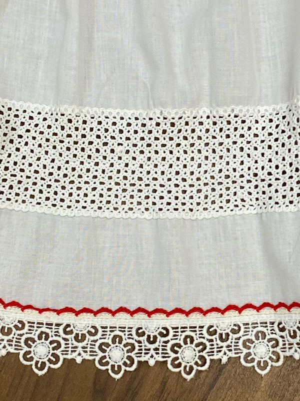 „Detailansicht Spitzenborte und rote Ziernaht an weißer Dirndlschürze“