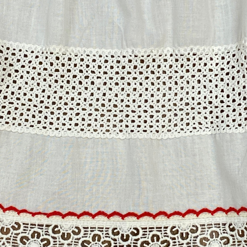 „Detailansicht Spitzenborte und rote Ziernaht an weißer Dirndlschürze“