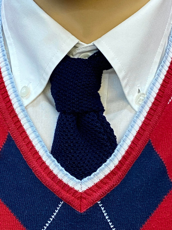 „Detailaufnahme 20er Jahre Herren Outfit mit dunkelblauer Strickkrawatte, weißem Hemd und rot-blauem Argyle Pullunder“