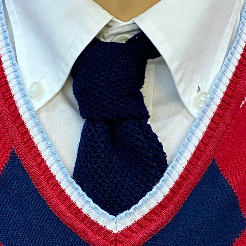 „Detailaufnahme 20er Jahre Herren Outfit mit dunkelblauer Strickkrawatte, weißem Hemd und rot-blauem Argyle Pullunder“