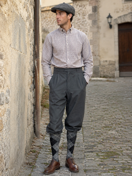 KI-generiertes Bild eines Vintage-Herren mit grauer Knickerbocker, kariertem Hemd, Rautenstrümpfen und Schiebermütze in einer historischen Altstadtgasse.