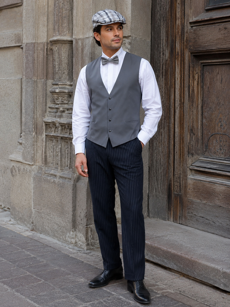 Mit KI erstelltes Bild eines Herren in Vintage-Outfit mit grauer Weste, weißem Hemd, gestreifter Fliege, Nadelstreifenhose und Schiebermütze vor historischer Fassade.