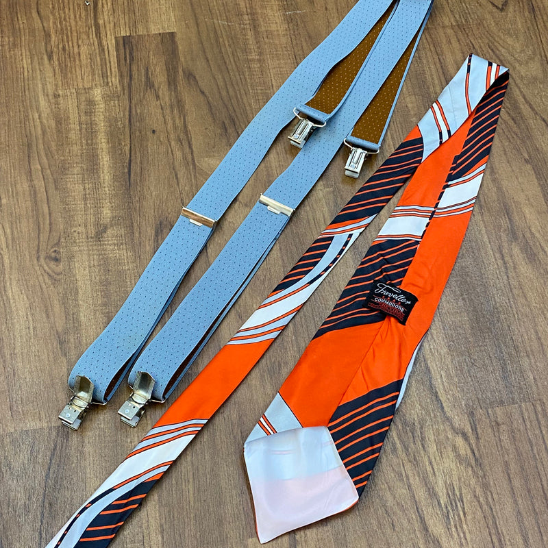 Vintage Accessoires für Herren – graue Hosenträger und rot-grau gestreifte Krawatte im Set, auf Holzuntergrund präsentiert.