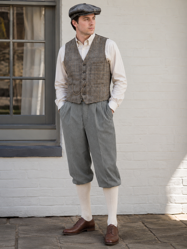 Herren Outfit im 20er Jahre Stil mit grauer Knickerbocker, karierter Weste, Hemd und Schiebermütze in heller Vintage-Umgebung