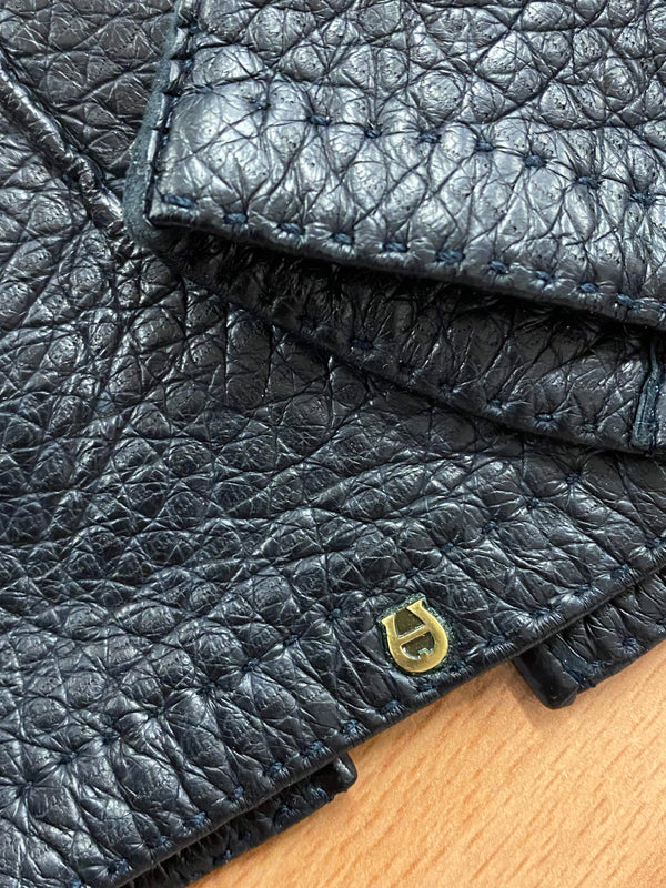 Detailaufnahme schwarzer Lederhandschuhe mit Ziernaht und goldenem Metall-Emblem