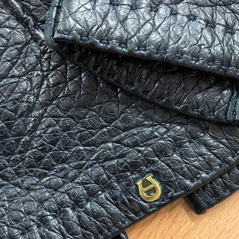 Detailaufnahme schwarzer Lederhandschuhe mit Ziernaht und goldenem Metall-Emblem