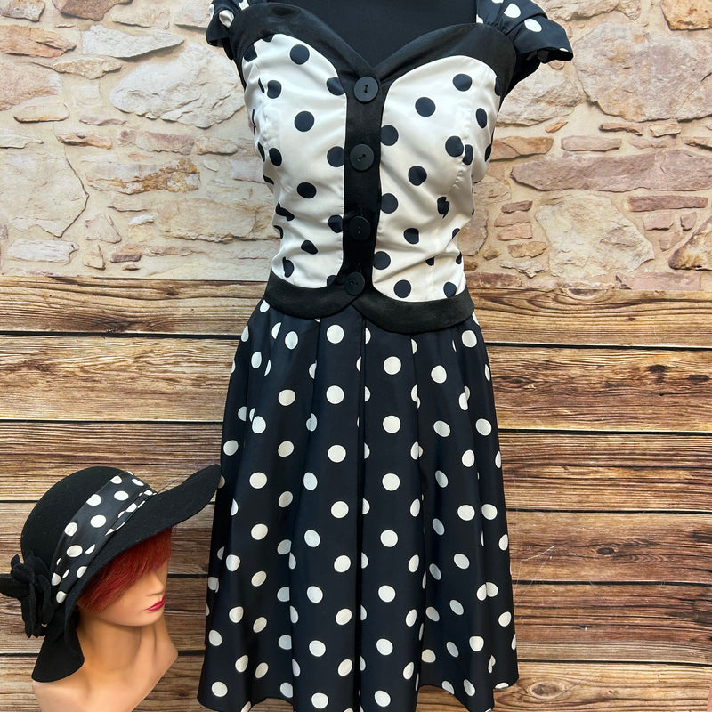 Vintage Damen-Punkte-Set: schwarz-weiß getupftes Oberteil mit Knöpfen und ausgestelltem Rock, schwarze Satinhandschuhe und schwarzer Filz-Cloche-Hut mit Punkte-Schleife