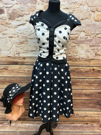 Vintage Damen-Punkte-Set: schwarz-weiß getupftes Oberteil mit Knöpfen und ausgestelltem Rock, schwarze Satinhandschuhe und schwarzer Filz-Cloche-Hut mit Punkte-Schleife