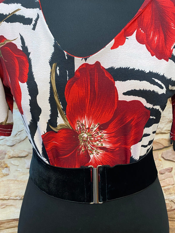 „Detailaufnahme Rockabilly Oberteil mit großer roter Blume, schwarz-weißem Muster und schwarzem Samtgürtel“