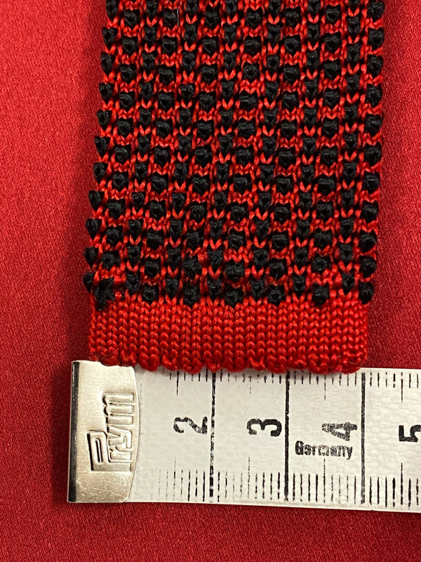 „Detailaufnahme gemusterte Strickkrawatte rot schwarz mit Massband“
