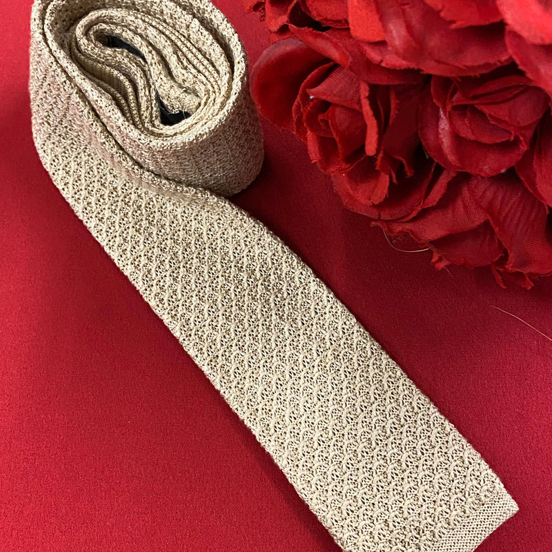 „Vintage Strickkrawatte beige auf rotem Hintergrund dekorativ drapiert“