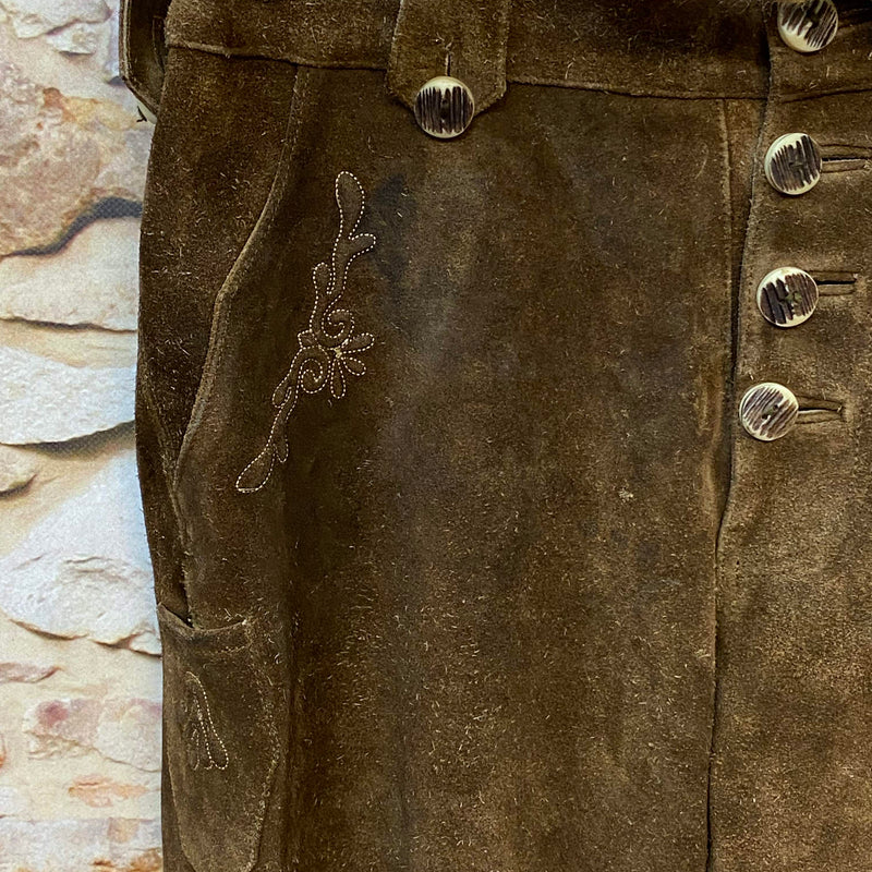 „Detailaufnahme dunkelbraune Trachtenlederhose aus Veloursleder mit Hornknöpfen und traditioneller Stickerei“