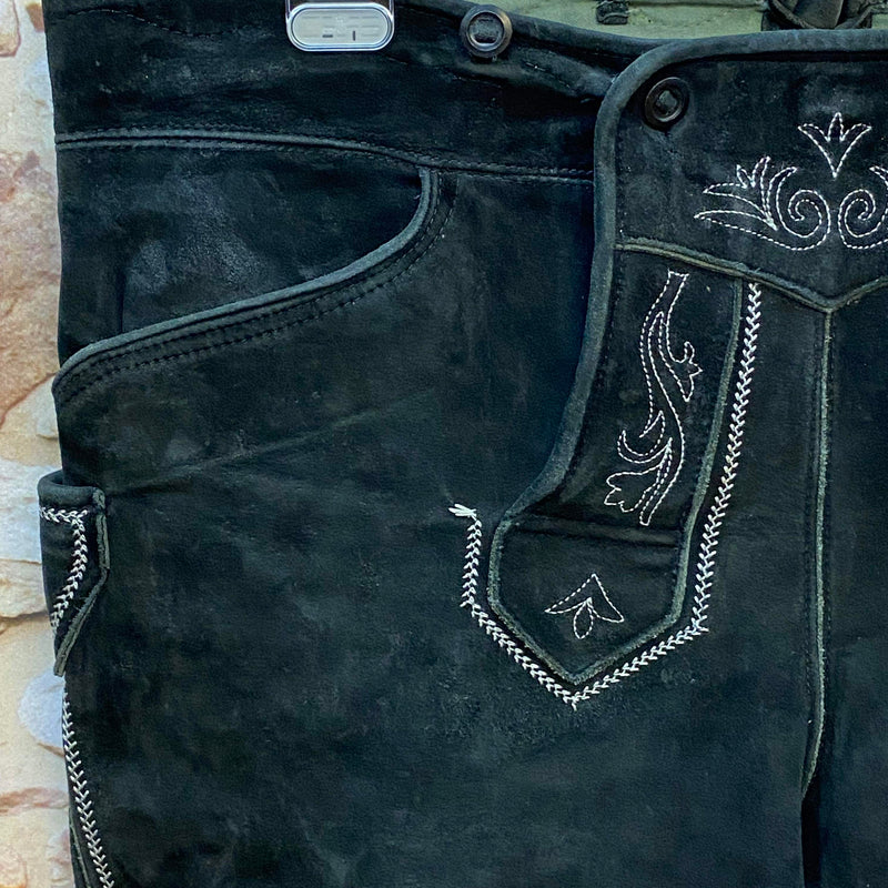 „Detailaufnahme schwarze Kniebund Trachtenlederhose mit traditioneller heller Stickerei am Latz“