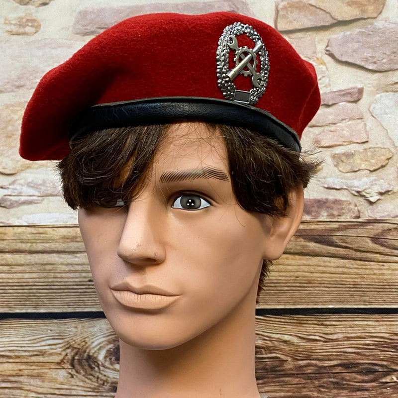 „Rotes Vintage Uniform-Barett Größe 60 mit schwarzem Rand und Metallabzeichen auf Schaufensterkopf“