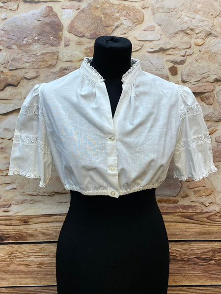 „Weiße Vintage-Dirndlbluse Hagro, Größe 42, mit Stehkragen, Knopfleiste und Spitzenborten an halblangen Puffärmeln, 1980er Jahre.“
