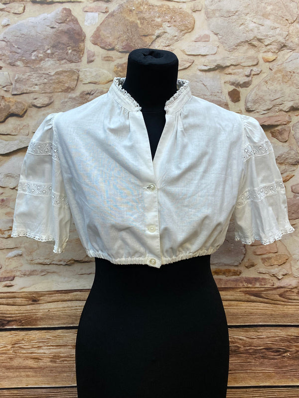 „Weiße Vintage-Dirndlbluse Hagro, Größe 42, mit Stehkragen, Knopfleiste und Spitzenborten an halblangen Puffärmeln, 1980er Jahre.“
