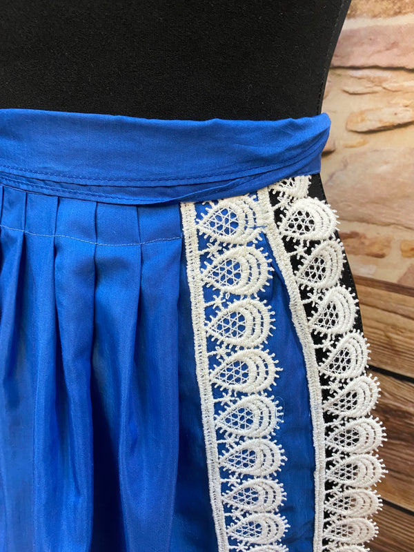 „Detailaufnahme: cremeweiße Bogen-Spitze an königsblauer Trachtenschürze.“