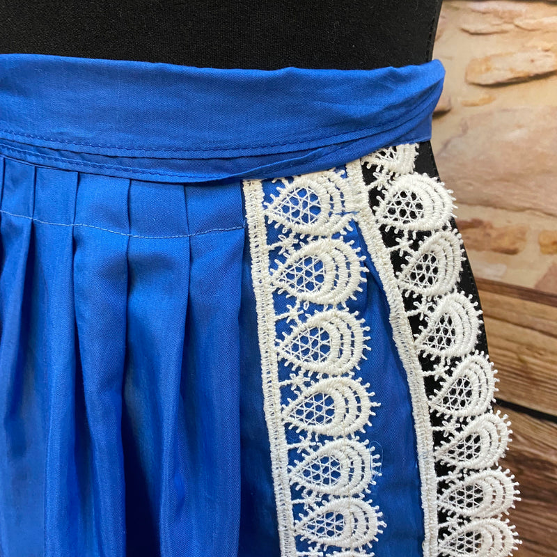 „Detailaufnahme: cremeweiße Bogen-Spitze an königsblauer Trachtenschürze.“