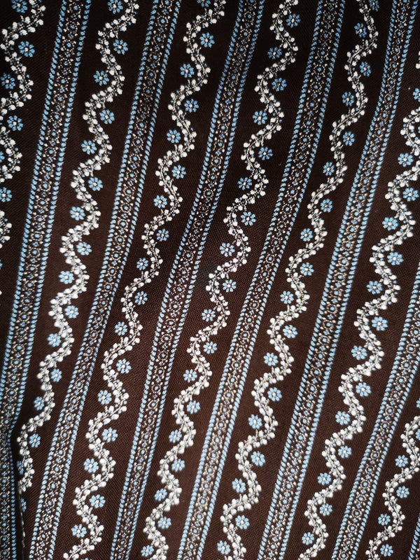 „Detailmuster der braun-blauen Baumwoll-Dirndlschürze mit floralen Streifen“
