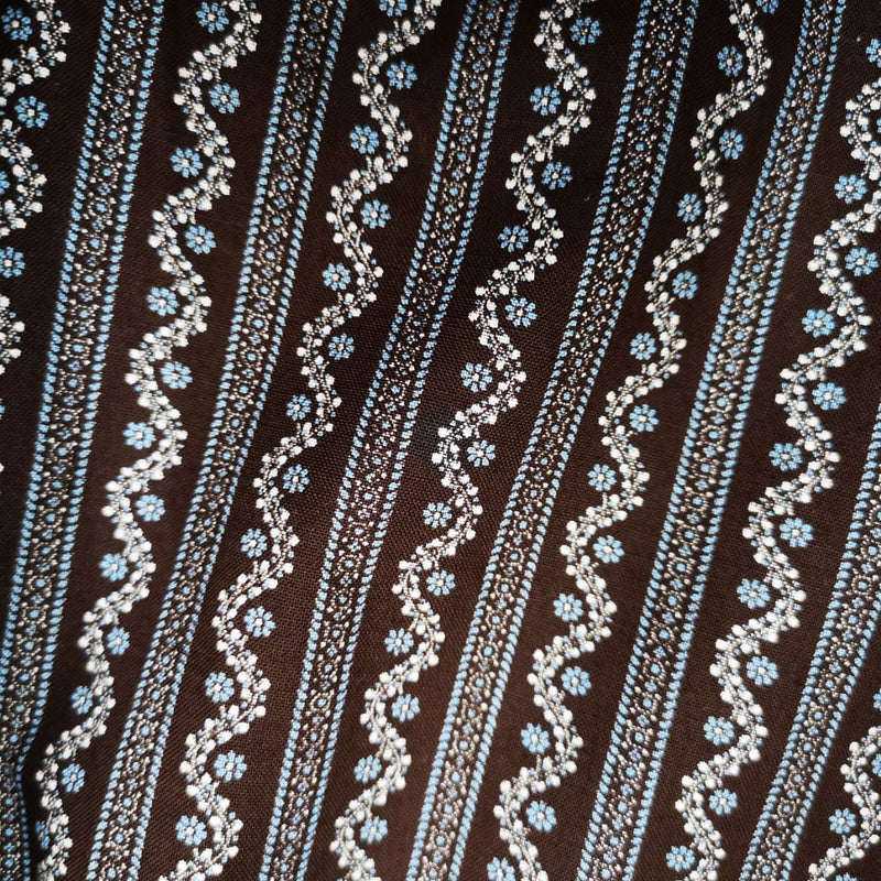 „Detailmuster der braun-blauen Baumwoll-Dirndlschürze mit floralen Streifen“