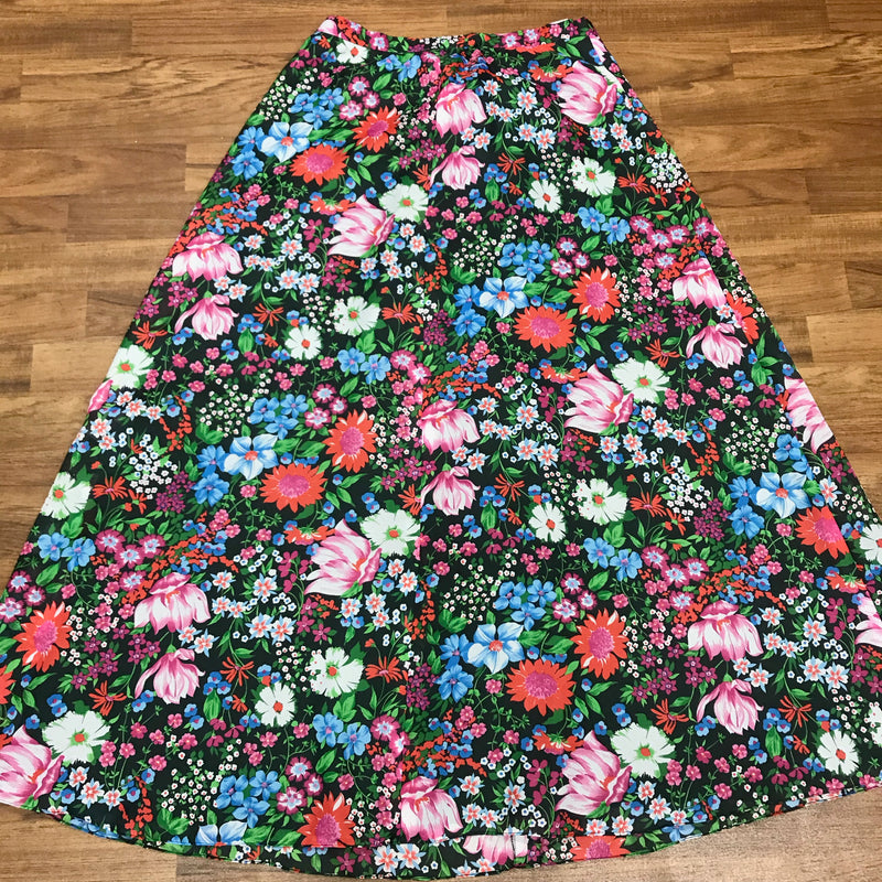 „Vintage Maxirock schwarz mit buntem Blumenprint ausgebreitet auf Holzboden“