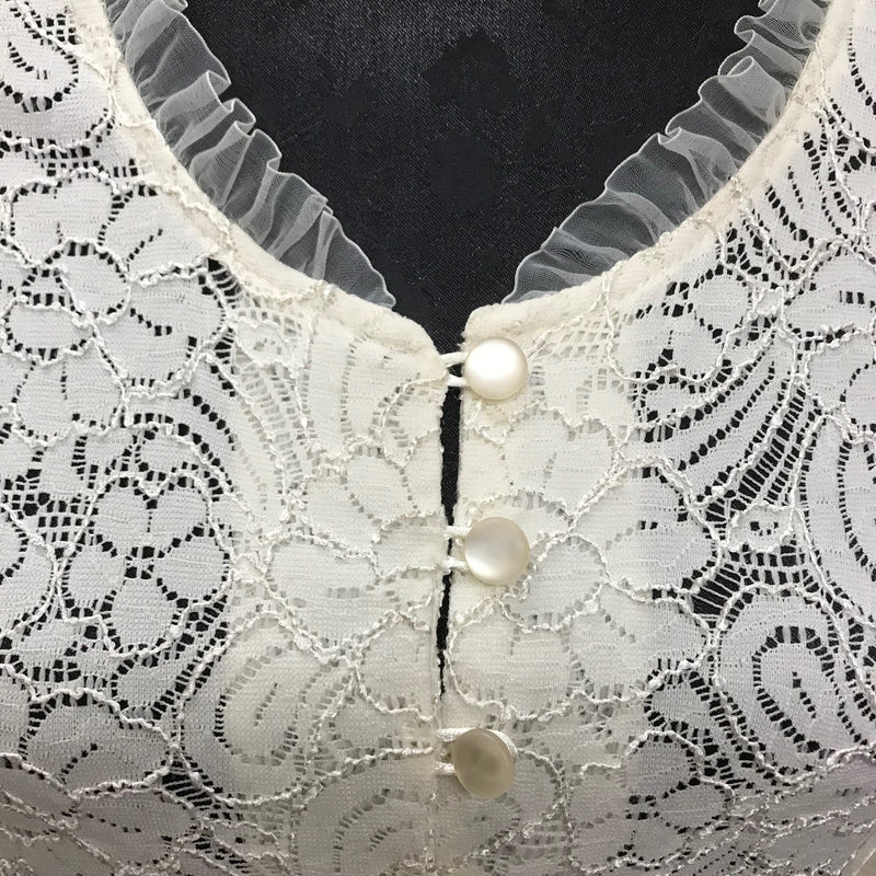 Detailaufnahme: Rüschen am Halsausschnitt und perlmuttartige Knöpfe der cremefarbenen Vintage-Spitzenjacke, feine florale Spitze