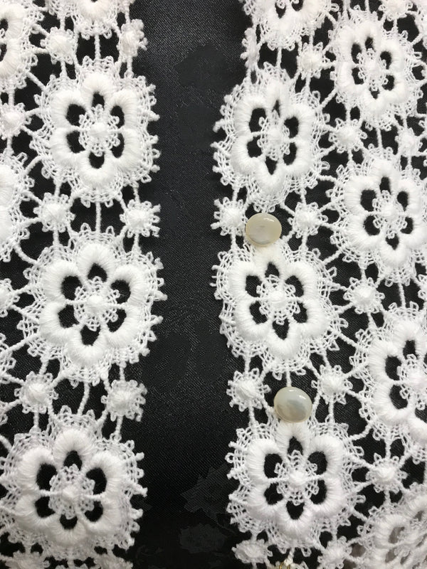 Detailaufnahme der cremefarbenen Häkelbluse mit Knöpfen und floraler Spitze.
