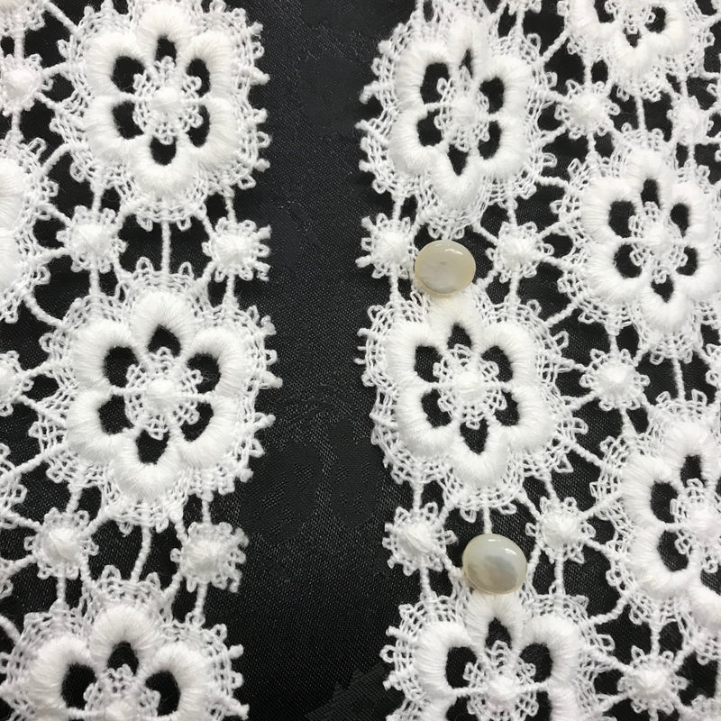 Detailaufnahme der cremefarbenen Häkelbluse mit Knöpfen und floraler Spitze.